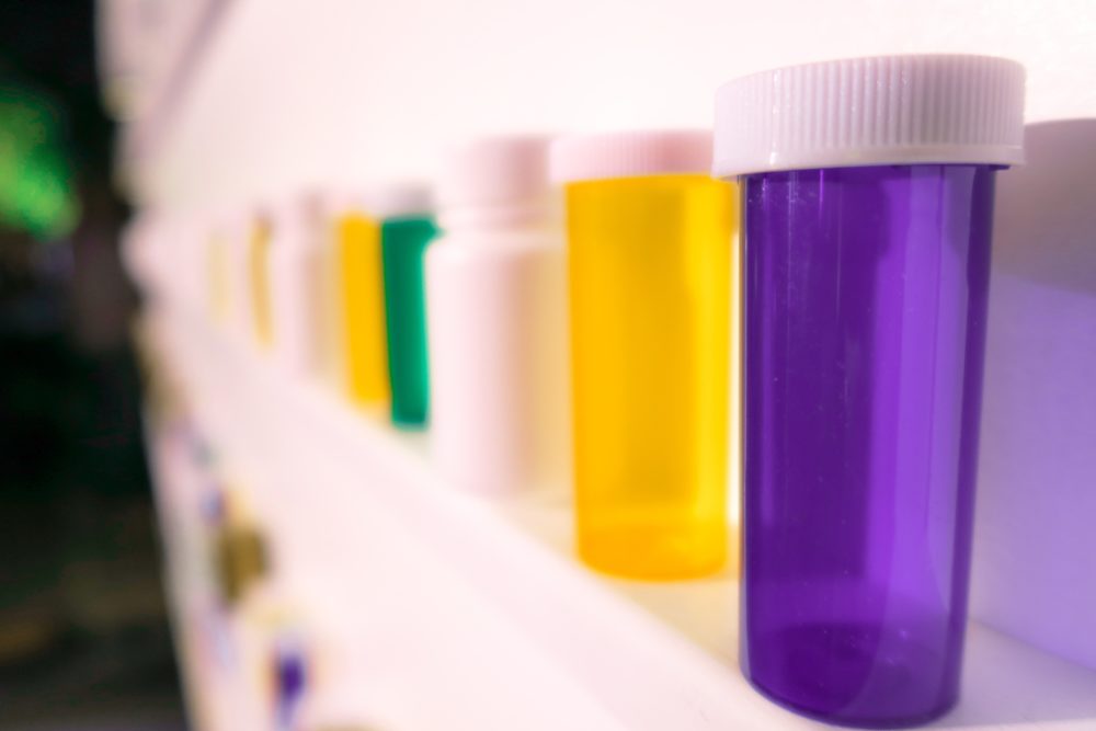 Purple, yellow, white and green pill boxes arranged in a line on a shelf