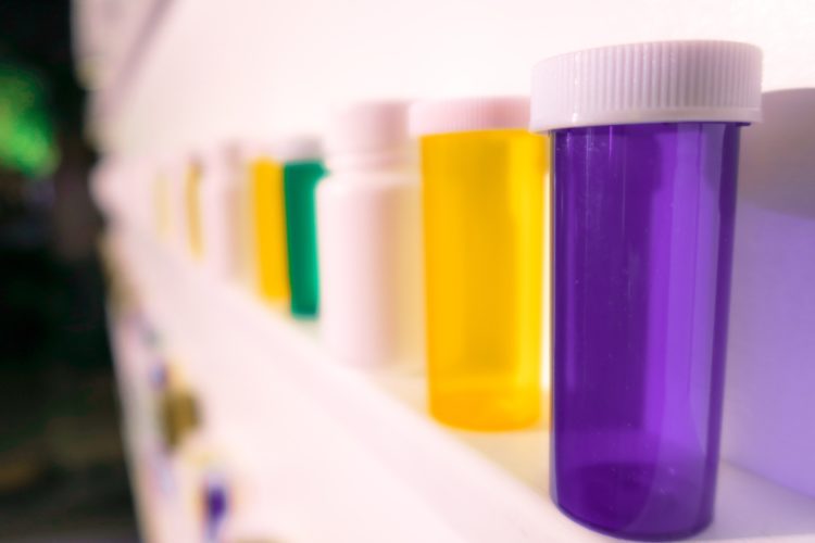 Purple, yellow, white and green pill boxes arranged in a line on a shelf