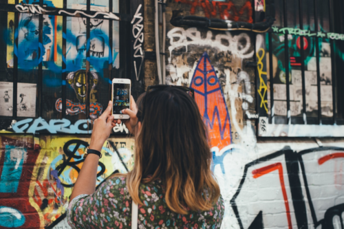 Picture of a woman taking a photo of street art on her phone.