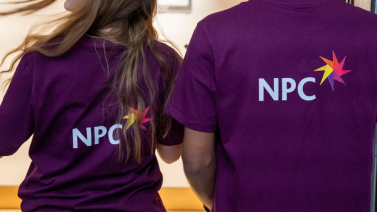 two NPC employees wearing purple t shirts that have the NPC logo on the back